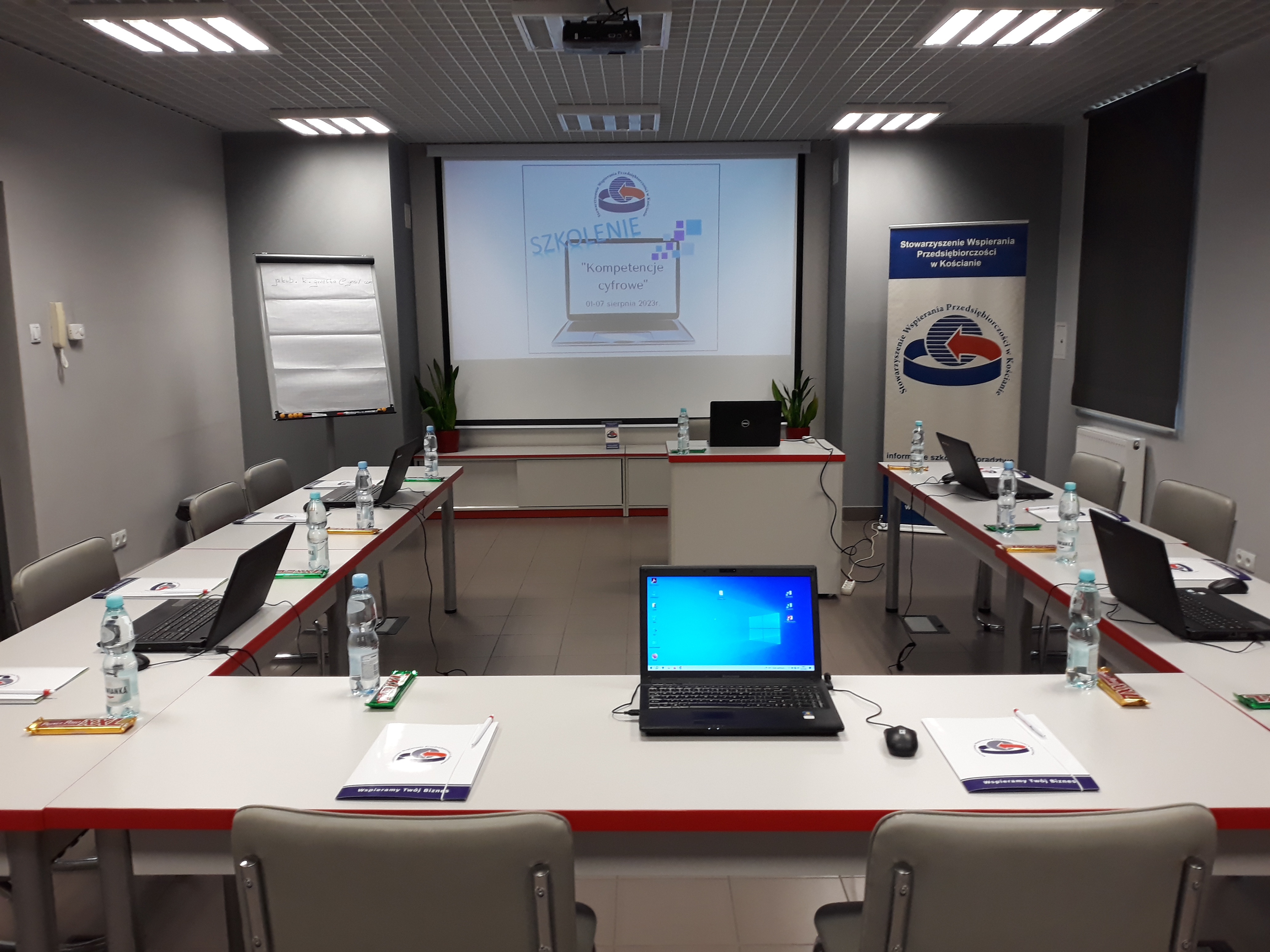 Sala w ośrodku wspierania przedsiębiorczości w Kościanie, ekran projektora oraz stanowiska szkoleniowe