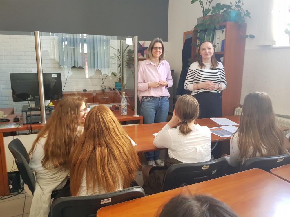 Pracownicy Powiatowego Urzędu Pracy w Kościanie prezentują uczniom spotkanie. Pracownicy są uśmiechnięci ustawieni przodem, uczniowie siedzą ustawieni tyłem lub bokiem.